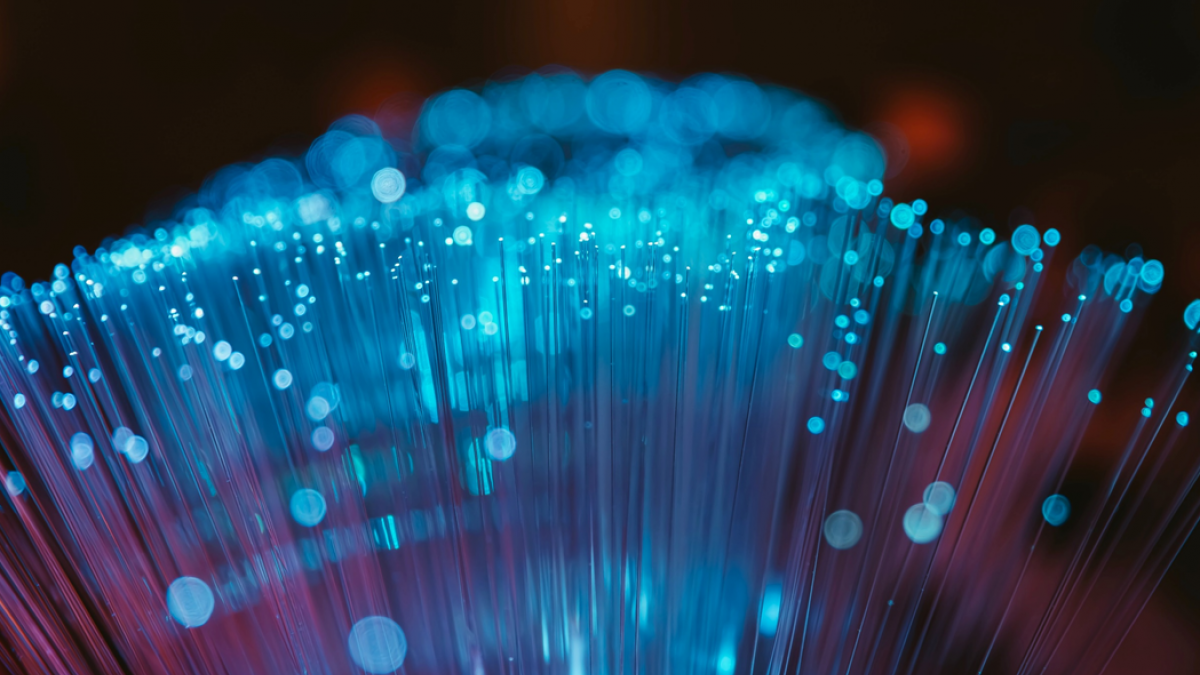 Photograph of a bundle of fiber optic strands glowing with blue light against a dark background.
