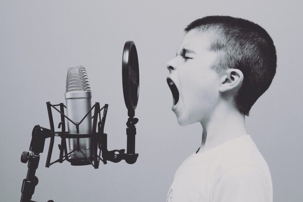 Black and white photograph of a boy shouting or singing loudly into a microphone.