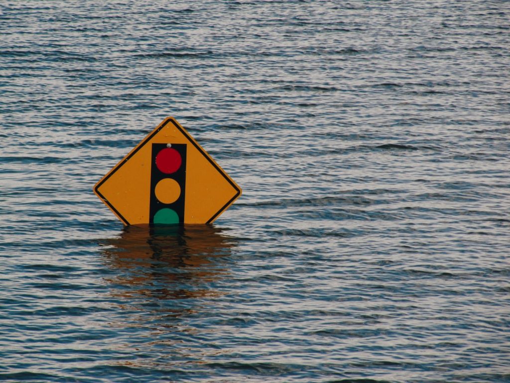 Photograph of flood waters partially submerging a road sign for a traffic signal.