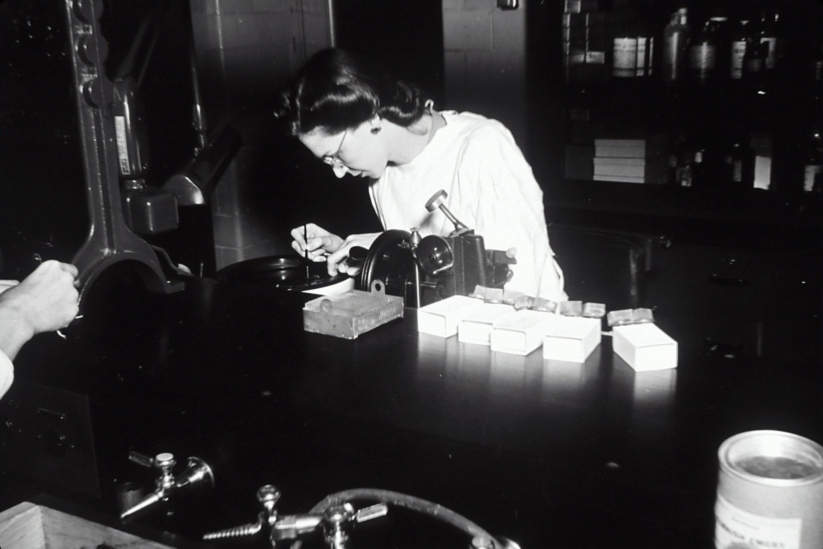 Black and white photograph of a woman working in a laboratory to prepare microscope slides.