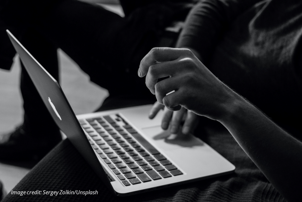 Closeup black and white photograph of an open laptop with hands poised to strike the keys. Image credit: Sergey Zolkin/Unsplash