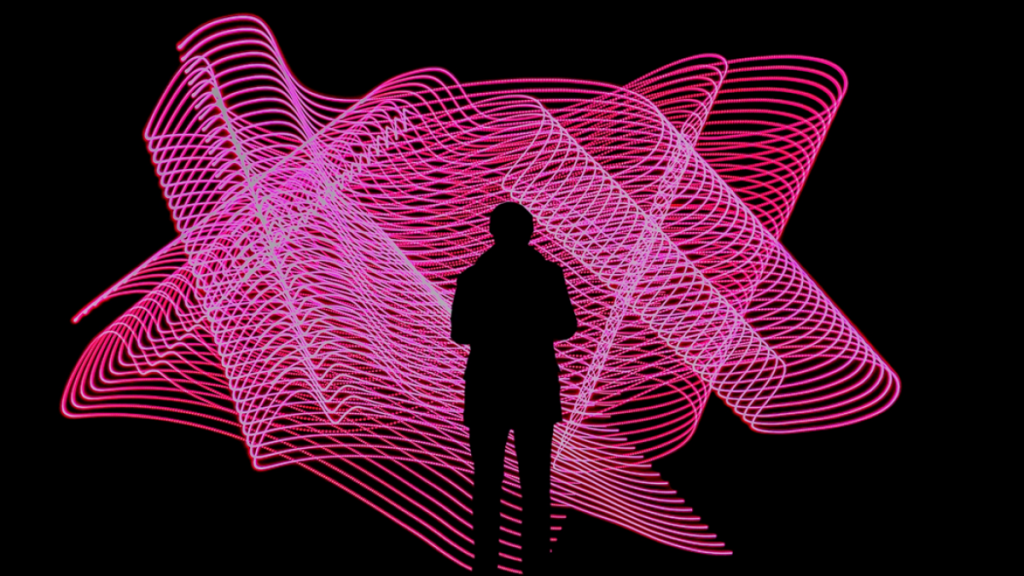 Photograph of person in silhouette against a brightly lighted abstract light display. Image credit: Fernand De Canne/Unsplash