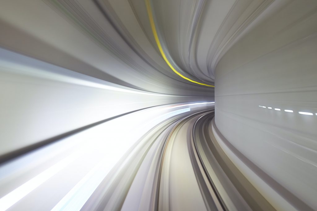 Time-lapse photograph with motion blur showing lights as a vehicle speeds through a curving tunnel. Image credit: Mathew Schwartz/Unsplash