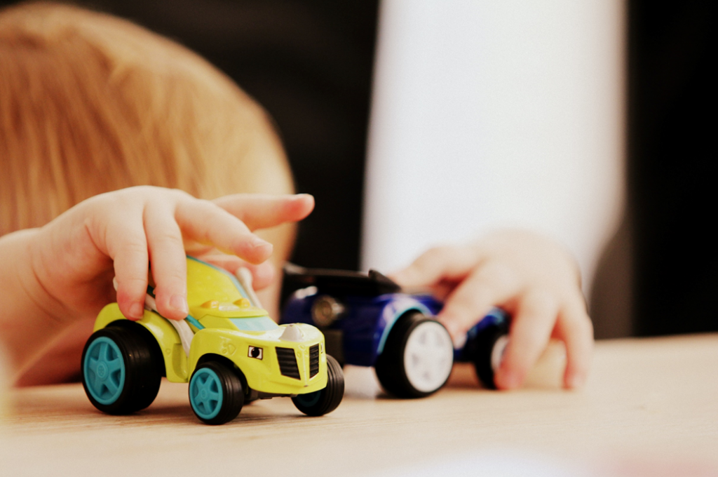 Photograph of a child (out of focus in background) playing with a pair of colorful toy racecars. Image credit: Sandy Millar/Unsplash