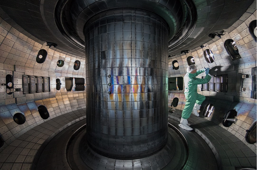Photograph of the interior of the donut-shaped reaction chamber in a tokomak fusion reactor, where gas plasmas are confined, pressurized, and heated to millions of degrees while being controlled with magnetic fields. Image credit: Rswilcox via Wikipedia (CC BY-SA 4).