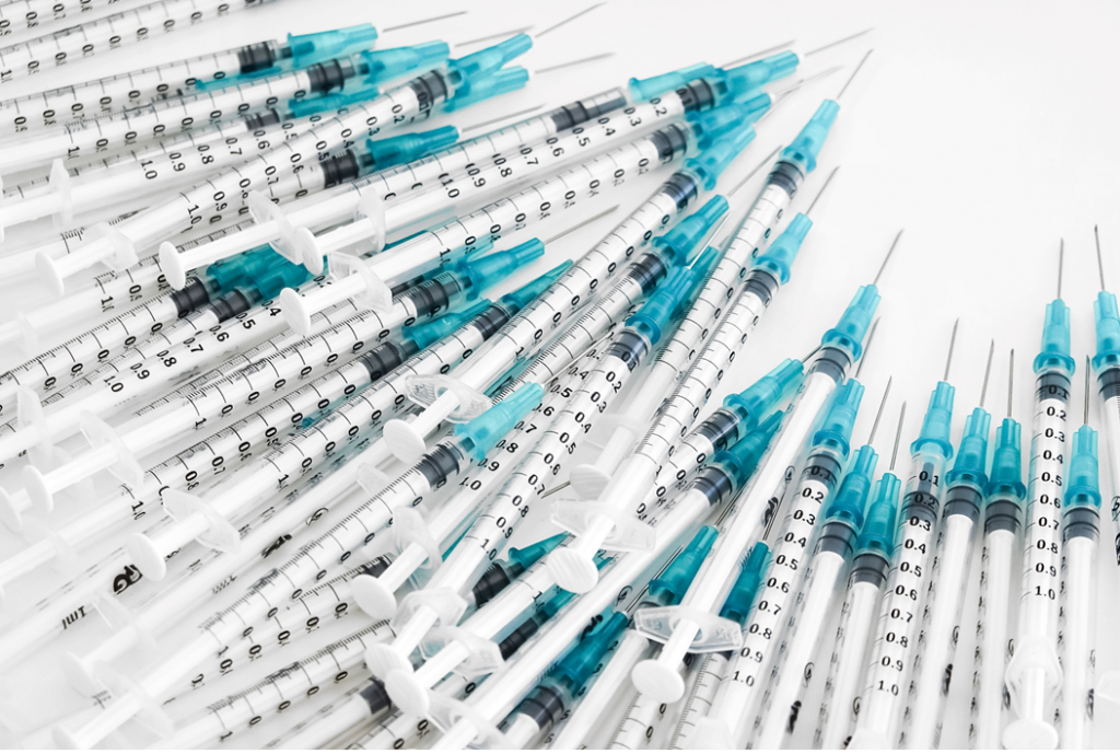 Photograph showing a pile of small syringes, white with blue at the tips. Image credit: Jeremy Bezanger/Unsplash