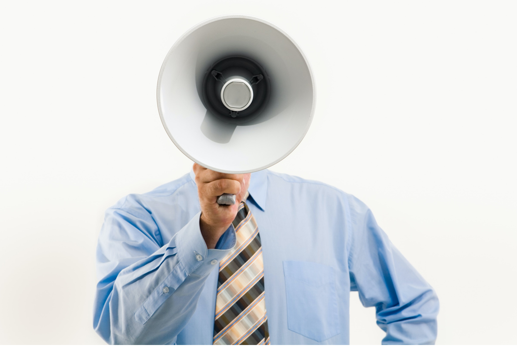 Man dressed in a button-down shirt and tie holding a megaphone directly in front of his face. Image credit: Pressmaster/Pexels