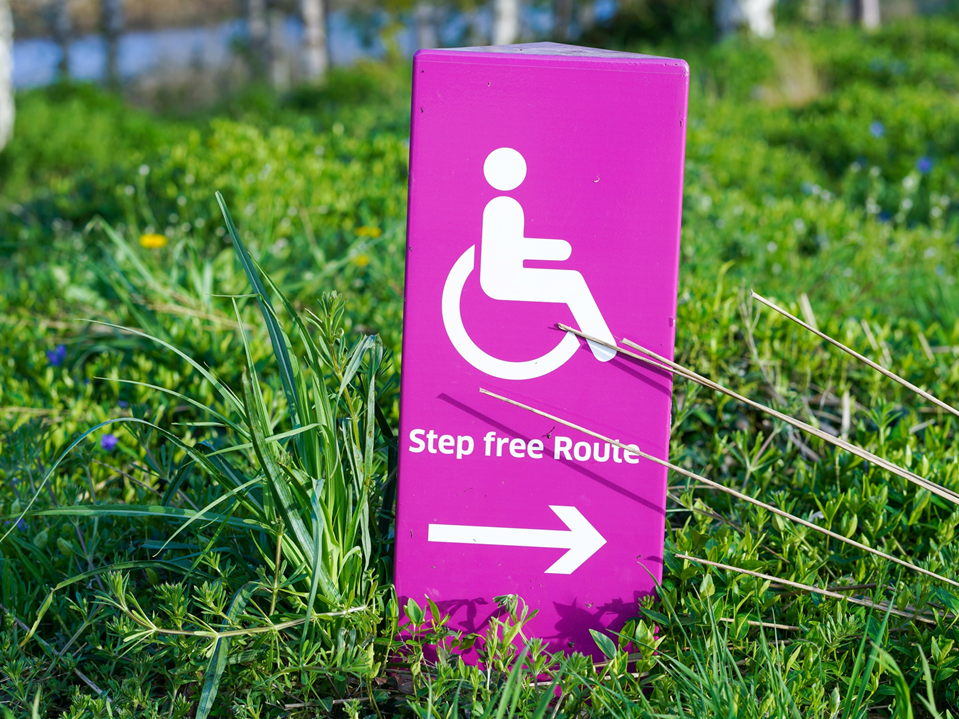 Photograph of a sign showing wheelchair symbol and directions to “step-free route.” Image credit: Yomex Owo/Unsplash