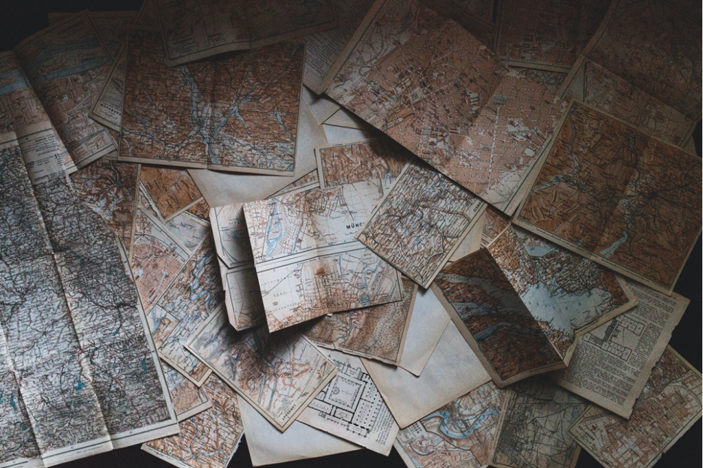 Photograph of multiple old maps in a disorderly pile on a flat surface. Image credit: Andrew Neel/Unsplash