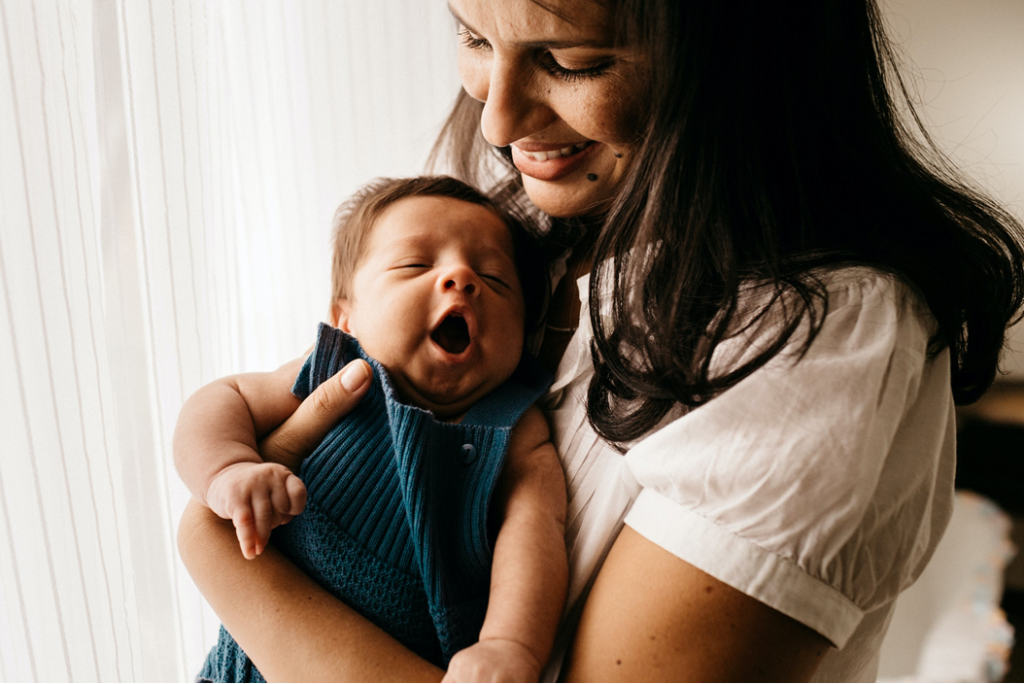 Photograph of smiling mother cradling yawning baby. Image credit: Jonathan Borba/Unsplash