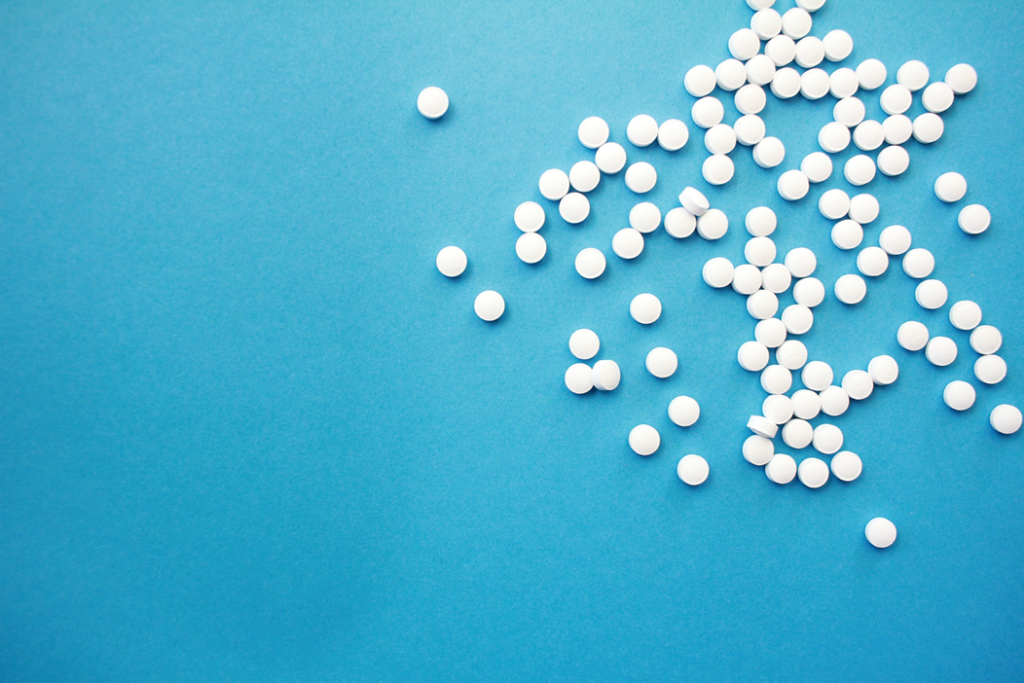 Small white pills scattered on a blue background. Image credit: Hal Gatewood/Unsplash