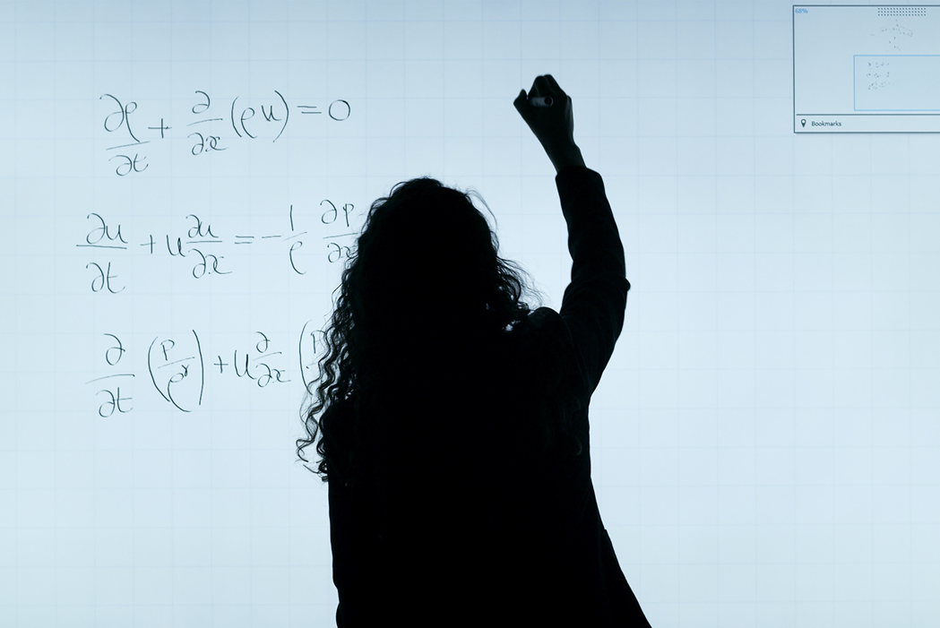 Silhouette of a woman writing equations on an illuminated board. Image credit: ThisisEngineering RAEng