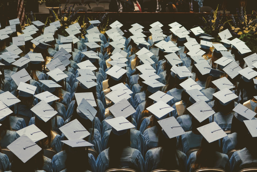Photograph from above and behind a group of seated students at commencement, with the students’ mortarboard hats obscuring their features. Image credit: Joshua Hoehne/Unsplash