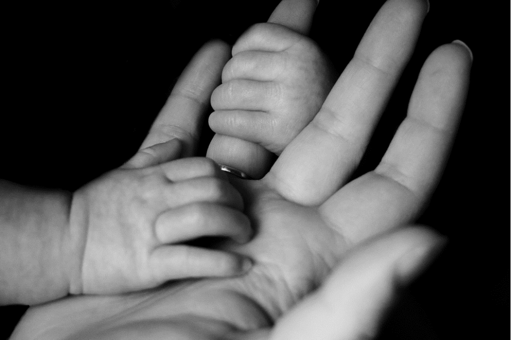 Close-up black and white photo of a tiny infant’s hands holding on to mother’s finger. Image credit: Liv Bruce/Unsplash