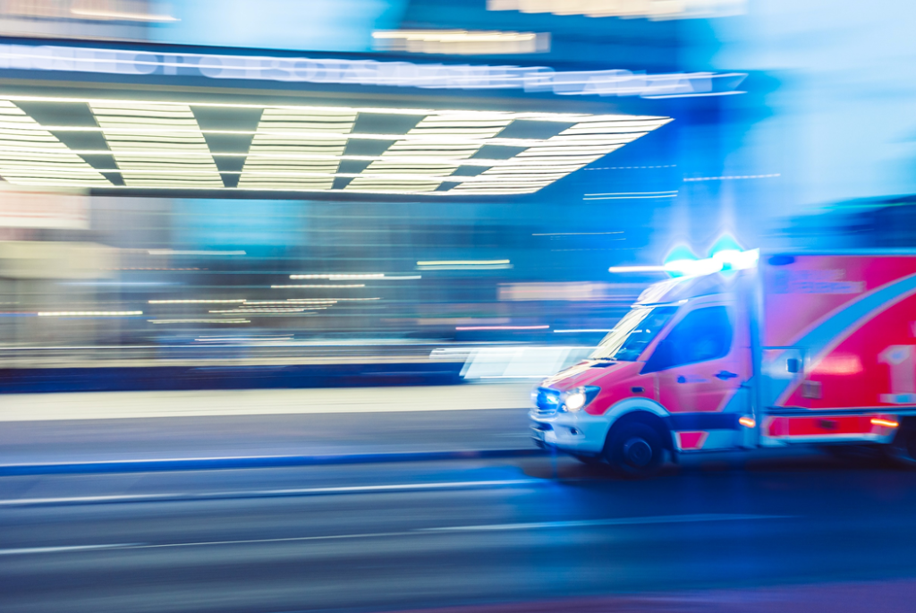 Motion-blurred photograph of an ambulance racing through city streets with its emergency lights on. Image credit: Camilo Jimenez/Unsplash