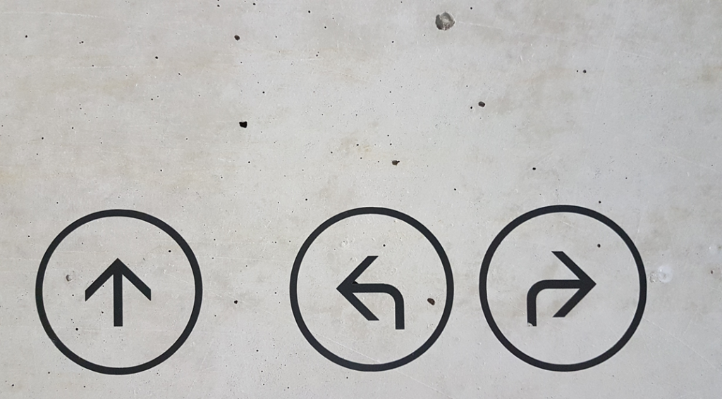 Photograph of directional signs (black paint on undressed concrete) with arrows enclosed in circles, with arrows pointing in different directions.Image credit: Marianne Bos/Unsplash
