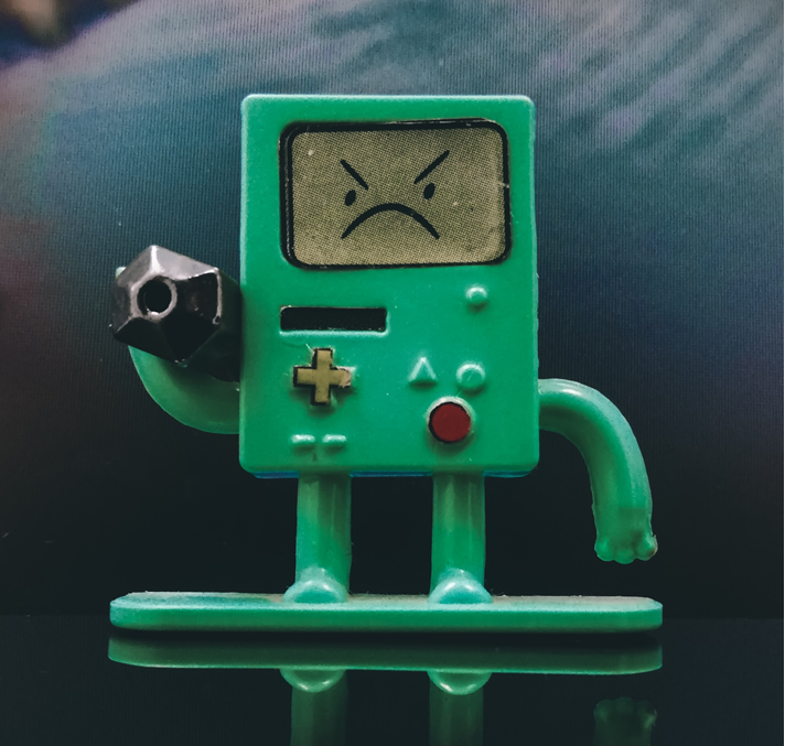 Small toy robot, shaped roughly like an MP3 player with arms and legs, with an angry, frowning expression on its face, apparently lifting a dumbbell. Image credit: Alejandro Mendoza/Unsplash