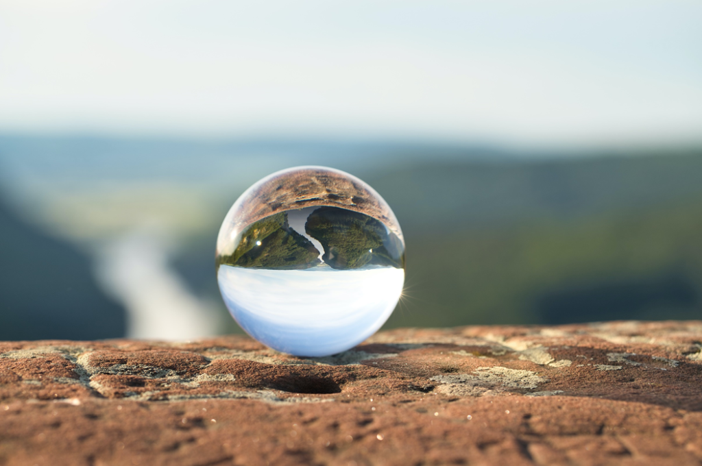 A selective photograph of a crystal ball, perched on a ledge or precipice, shows the landscape below refracted and inverted. Image credit: March Schulte/Unsplash