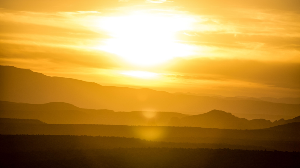 Photograph showing sun, blurred by clouds, setting behind ranges of hills. Image credit: Scott Goodwill/Unsplash