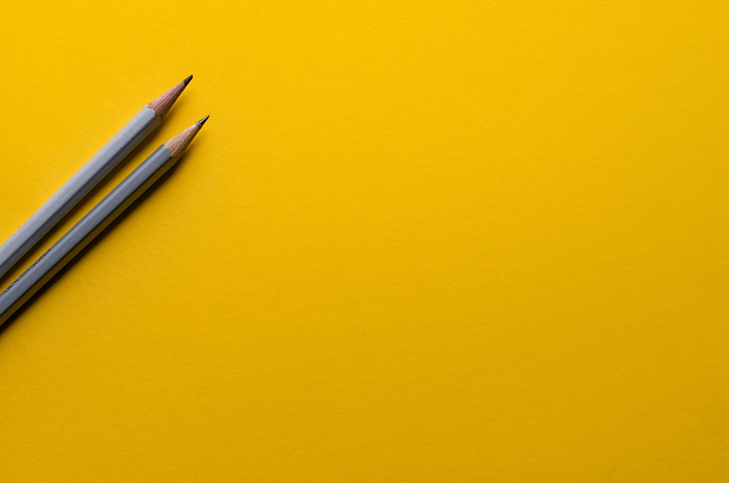 Close-up photograph of two sharpened grey pencils lying at a slant on a yellow background. Image credit: Joanna Kosinska/Unsplash