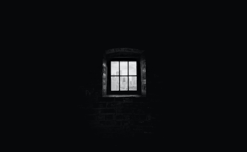 Picture of window with a view of distant city skyline, taken at some distance back in a darkened room. Image credit: Ed Vázquez/Unsplash