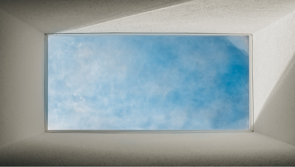 Picture, taken from below, showing a skylight window opening on to blue sky with wispy white clouds. Image credit: Dylan Ferreira/Unsplash