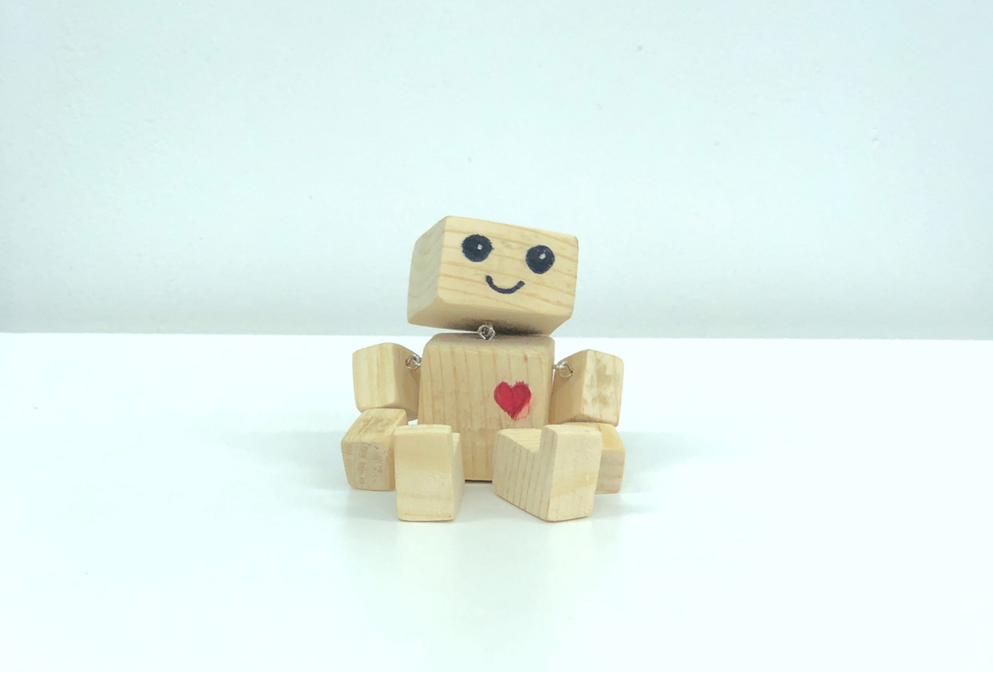 A small toy robot made out of wooden blocks, seated on a flat surface, with a smiling expression and a red heart shape on its chest. Image credit: Ochir-Erdene Oyunmedeg/Unsplash