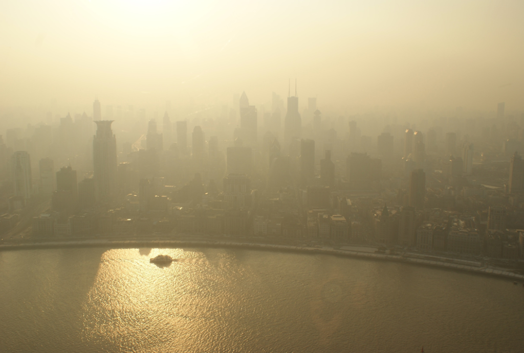 Aerial photograph of a city skyline and waterfront, with skyscrapers and other building enveloped in smog and haze. Image credit: Alex Gindin/Unsplash