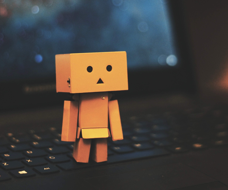 A small toy robot constructed out of boxy shapes stands on the keyboard of an open laptop computer, facing the camera. Image credit Jem Sahagun/Unsplash