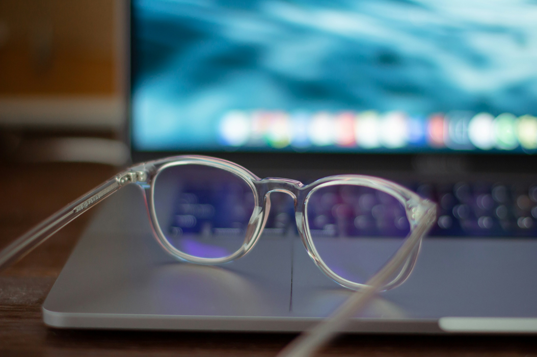 A pair of round eyeglasses with transparent frames rests on an open laptop, with screen visible out of focus in the background. Image credit: K8/Unsplash