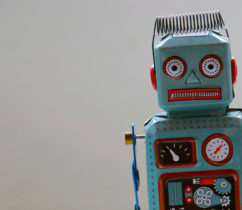 Close-up photo of old-fashioned tin toy robot, posed facing the camera, with a strangely chagrined look on its face. Image has been cropped from right relative to original. Image credit: Rock’n roll Monkey/Unsplash