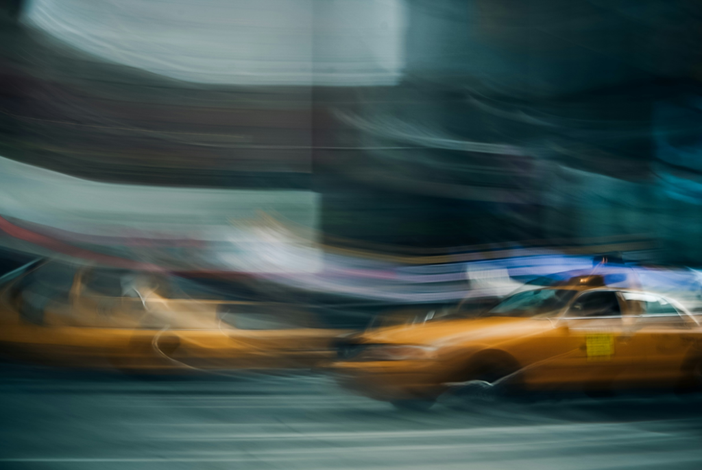 Motion-blurred photograph of taxis on a city street, with what appears to be a dark building in the background. Image credit: Scott Umstattd/Unsplash