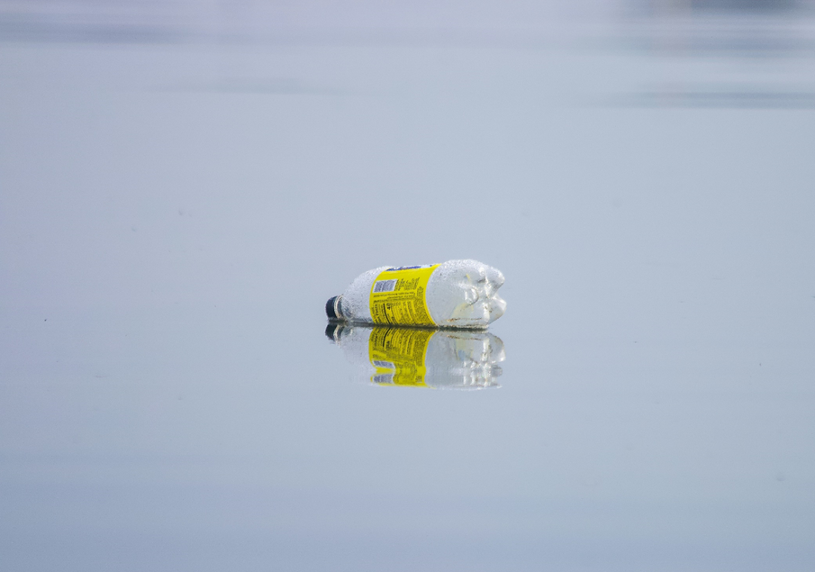 A discarded, empty plastic bottles lies on a sandy beach at the tide line. Image credit: Brian Yurasits/Unsplash