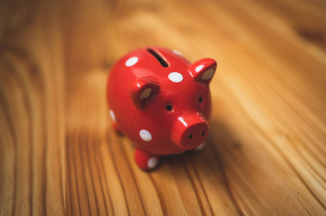 A red piggy bank with white polka dots sits on top of a wooden table. Image credit: Andre Taissin/Unsplash