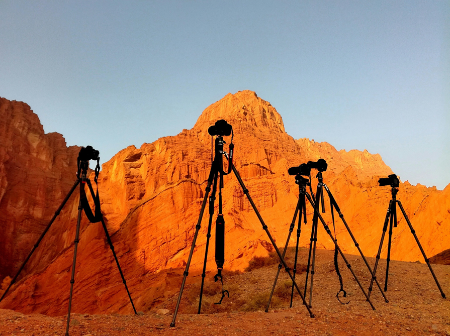 Multiple black tripods with cameras on top are clustered together in front of a desert rock formation, with blue skies in the background. Image credit: Richard Lee/Unsplash