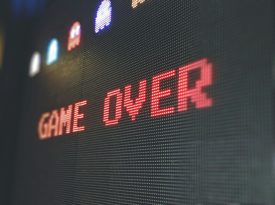 Pixellated text declaring “GAME OVER,” red on a black background, from the final screen of an arcade video game. Image credit: Rivage/Unsplash