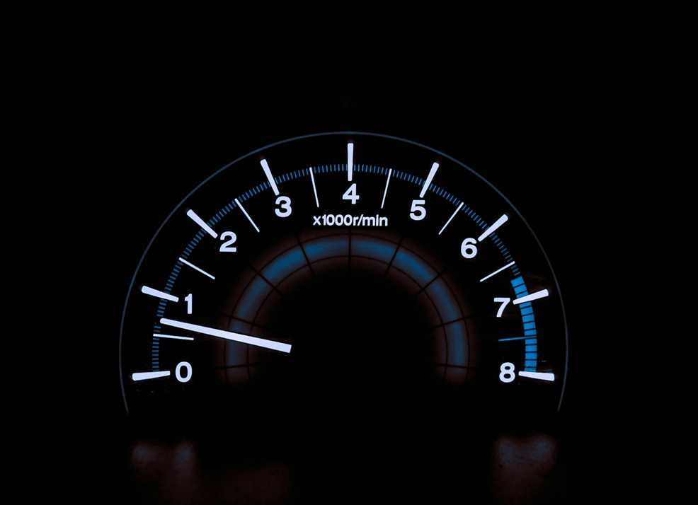 Closeup photograph of a car’s backlit dashboard tachometer, with the indicator needle sitting just above the idle mark between 0 and 1 x1000 RPM. Image credit: Chris Liverani/Unsplash