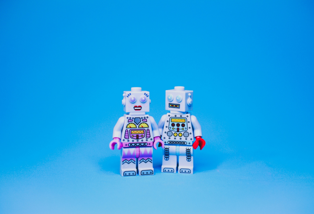 A pair of Lego robots, one “male” and one “female”, stand close to each other, the male report turned slightly to face the female robot. Image credit: Nik/Unsplash