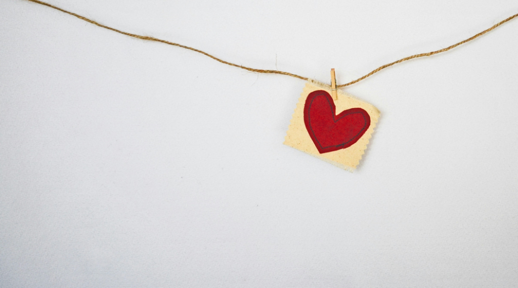 Red heart shape drawn on rough paper or fabric is pinned to a piece of twine. Image credit: Debby Hudson/Unsplash