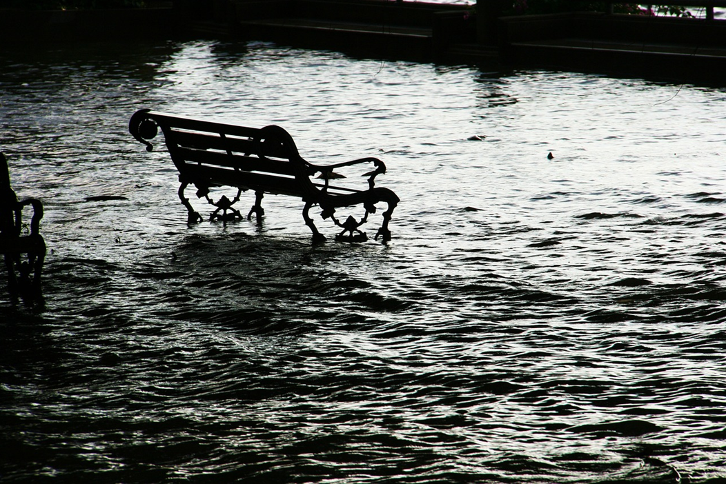 Black and white photograph showing a park bench surrounded by flood water. Image credit: Dean Moriarty/Pixabay