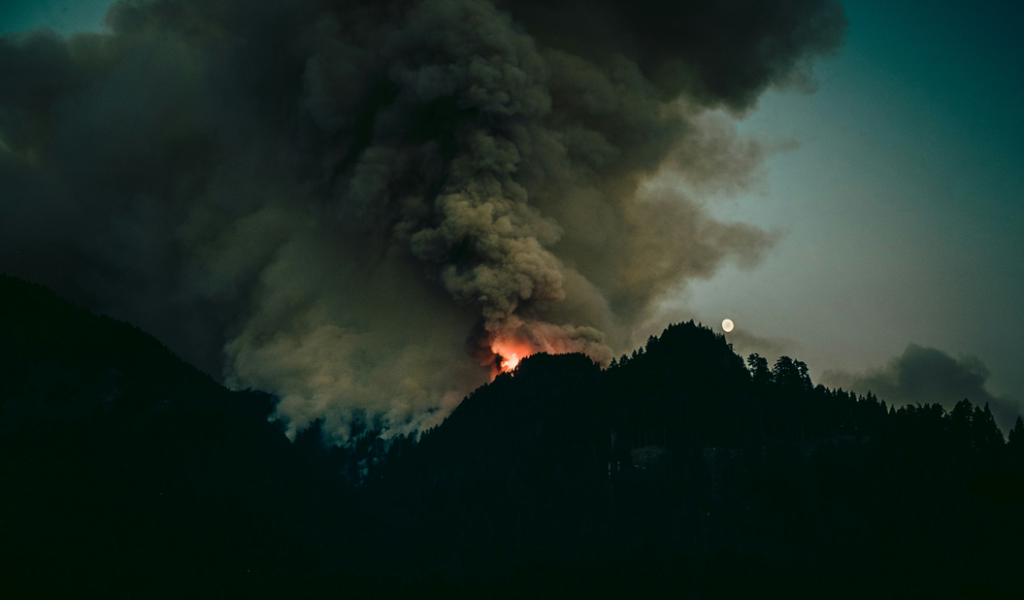 Photograph showing plumes of smoke rising from a wildfire on mountain ridges. Image credit: Luke Flynt/Unsplash.