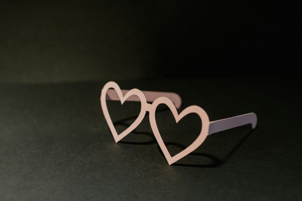 A pair of cardboard novelty glasses with heart-shaped frames sitting on a dark background. Image credit: Kelley Sikkema/Unsplash