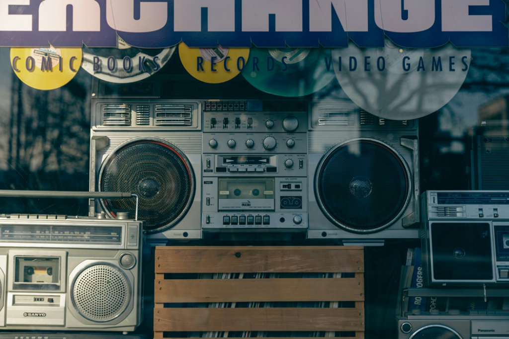 Portable “boombox” stereos sitting behind a display window in a music shop. Image credit: Nellie Adamyan/Unsplash