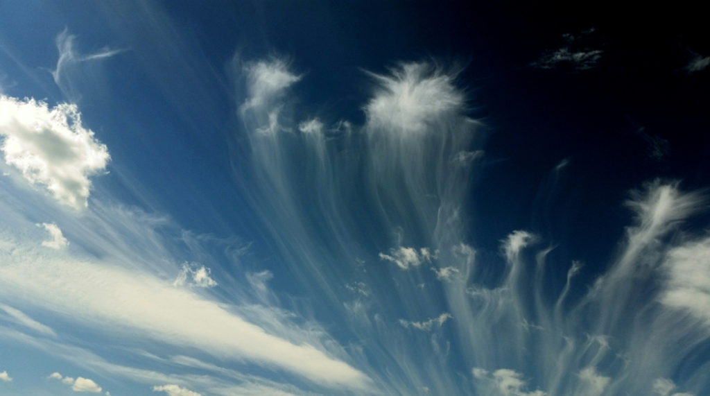 Photograph of blue sky showing high, wispy cirrus clouds streaming out as if being blown by high winds. Image credit: NOAA