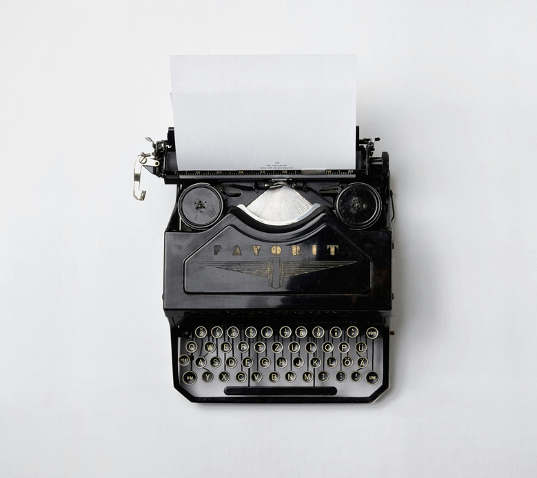 Photograph taken from above of an old fashioned mechanical typewriter with a black metal case and a sheet of blank paper inserted. Image credit: Florian Klauer/Unsplash