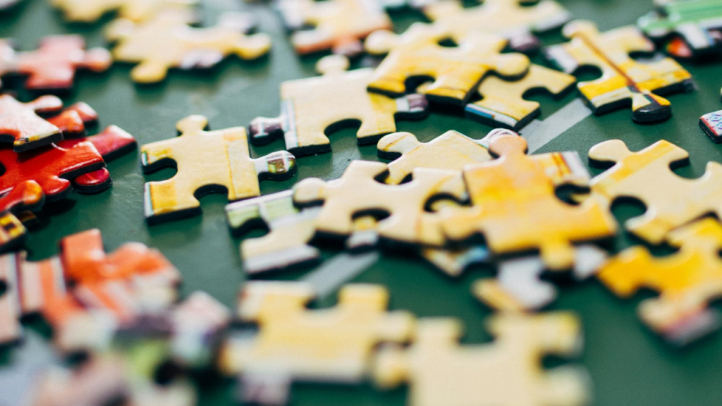 Selective focus photograph shows a disorderly pile of jigsaw puzzle pieces lying on a flat surface. Image credit: Nathalia Segato/Unsplash