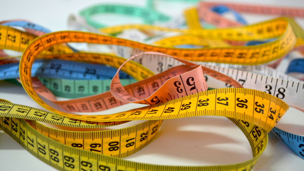 Close-up photograph shows a tangle of colorful measuring tapes, some marked in inches, others in centimeters. Image credit: Patricia Serna/Unsplash