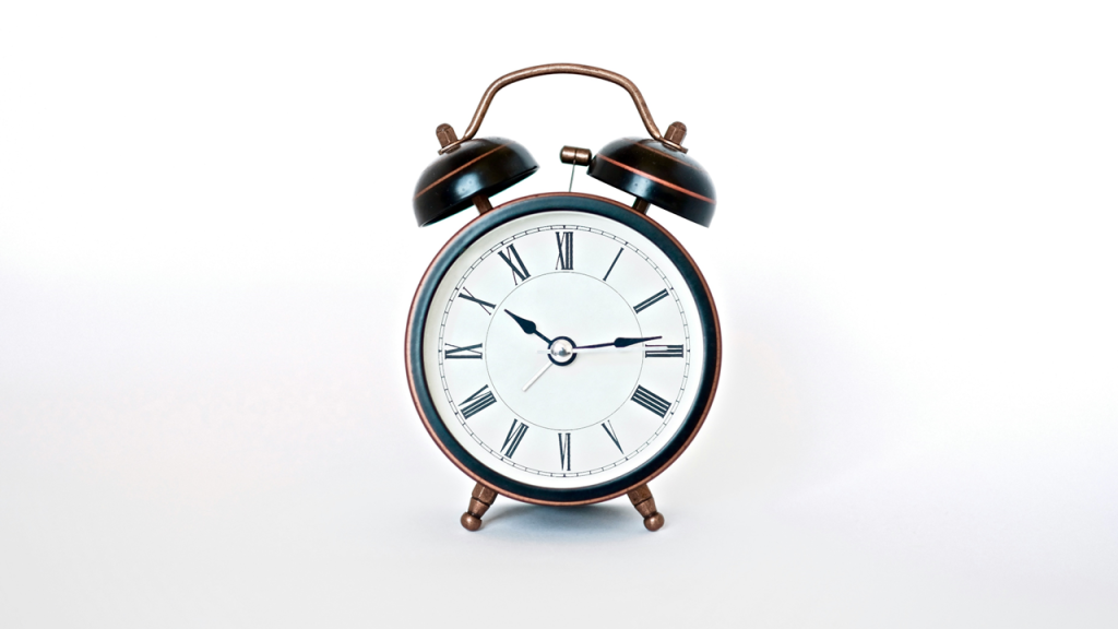 An old-fashioned analog double-bell alarm clock with Roman numerals on the clock face stands against a light background. Image credit: Insung Yoon/Unsplash