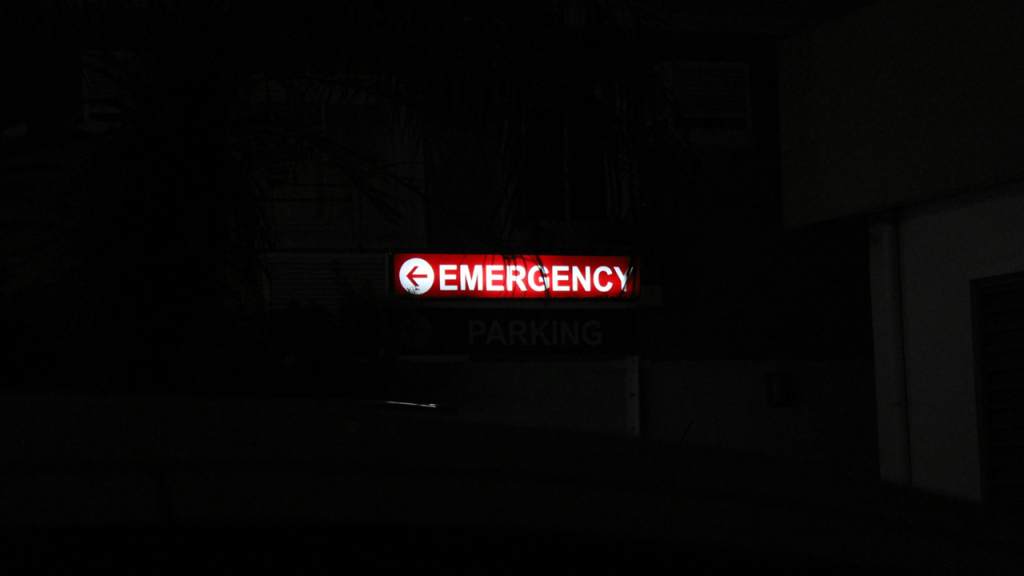 Lighted outdoor sign with the word EMERGENCY in white letters and a directional arrow against a dark background. Image credit: Jake/Unsplash